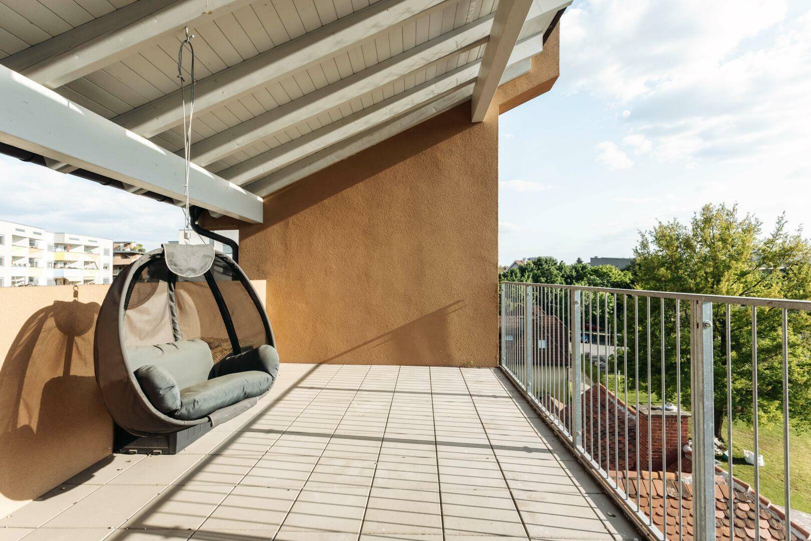 Sonnige Terrasse mit Fliesenboden, Hängesessel und weitem Blick auf die Umgebung.