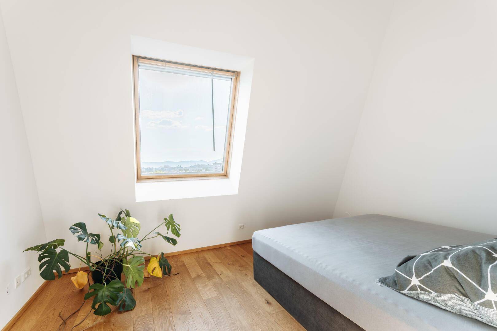 Schlafzimmer mit Holzboden, einem bequemen Bett und viel Tageslicht durch das Dachfenster.