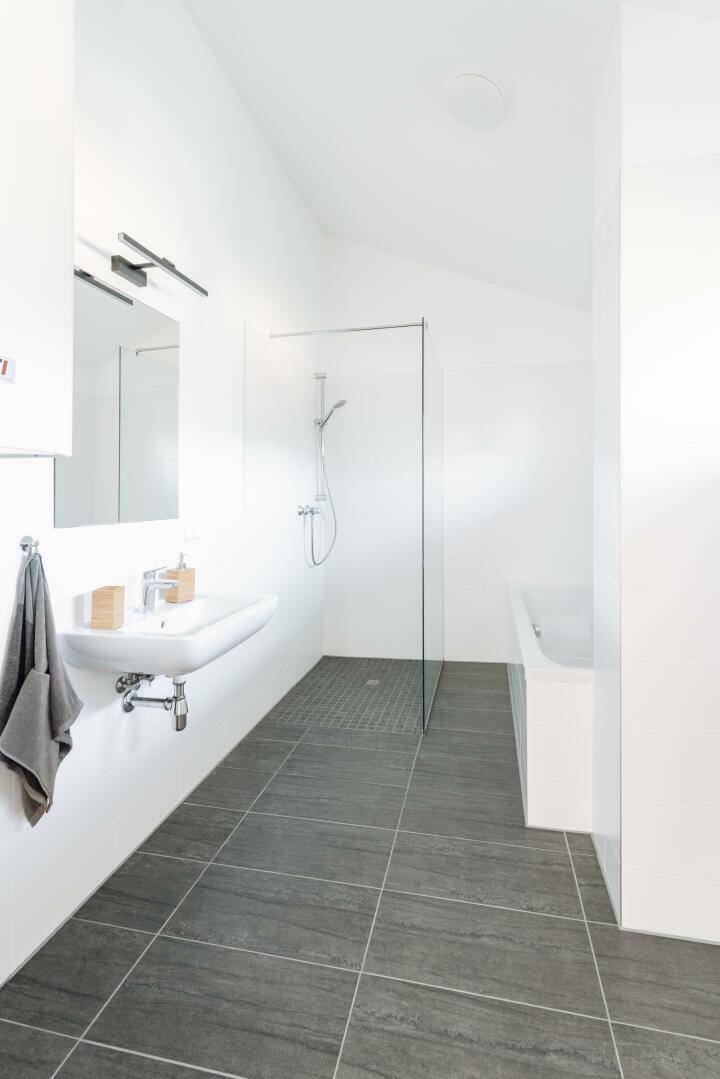 Modernes Badezimmer mit dunklen Fliesen, begehbarer Dusche und einer Badewanne.