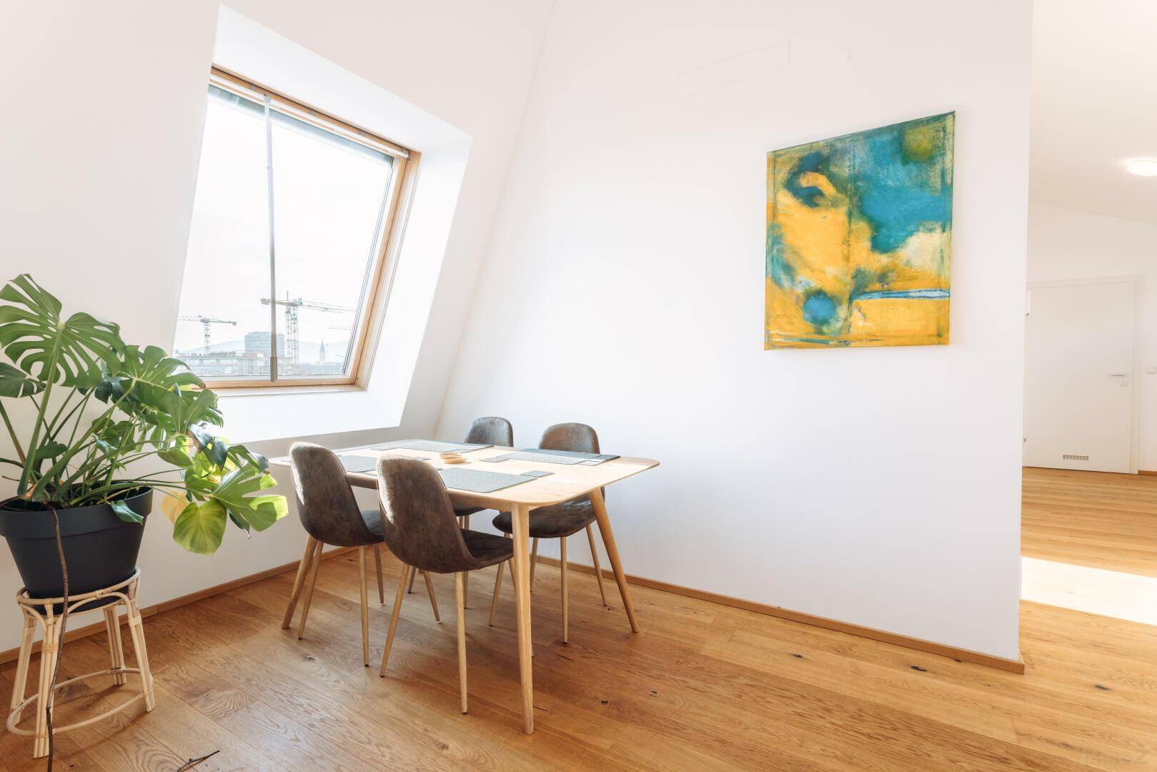 Heller Essbereich mit Holzboden, modernem Tisch und Stühlen unter einem Dachfenster.