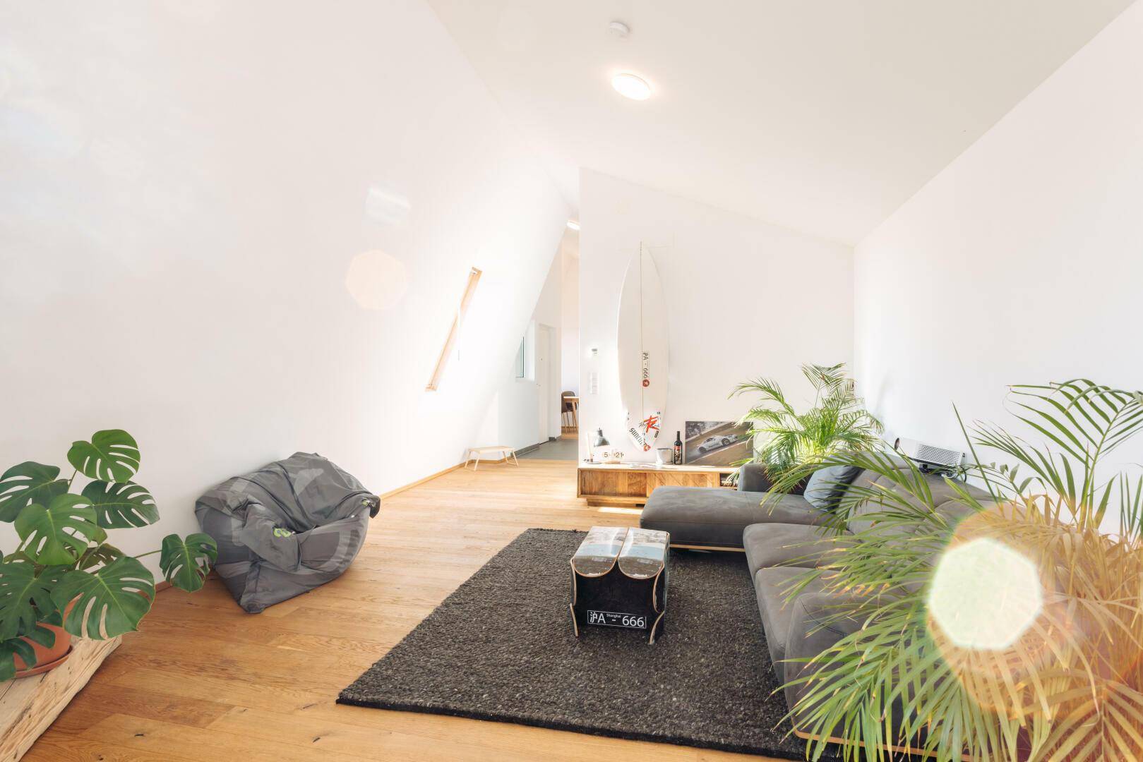 Helles und offenes Wohnzimmer mit Holzboden, bequemer Couch und dekorativen Pflanzen.