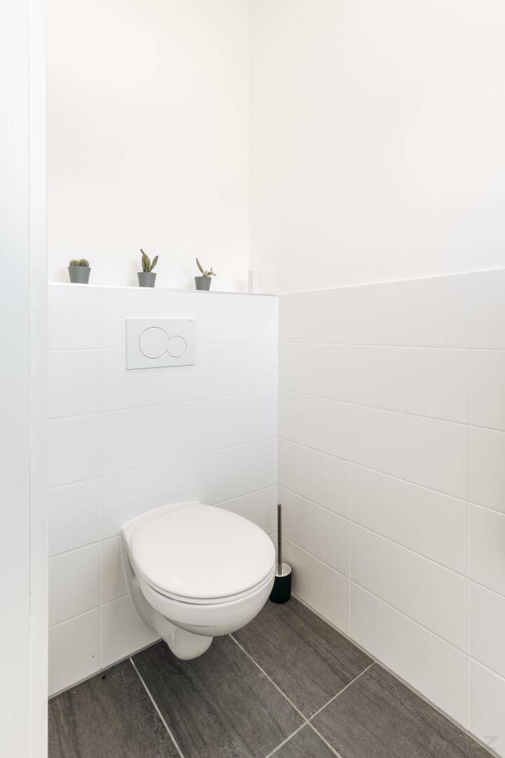 Sauberes Gäste-WC mit wandhängender Toilette und dunklen Bodenfliesen.
