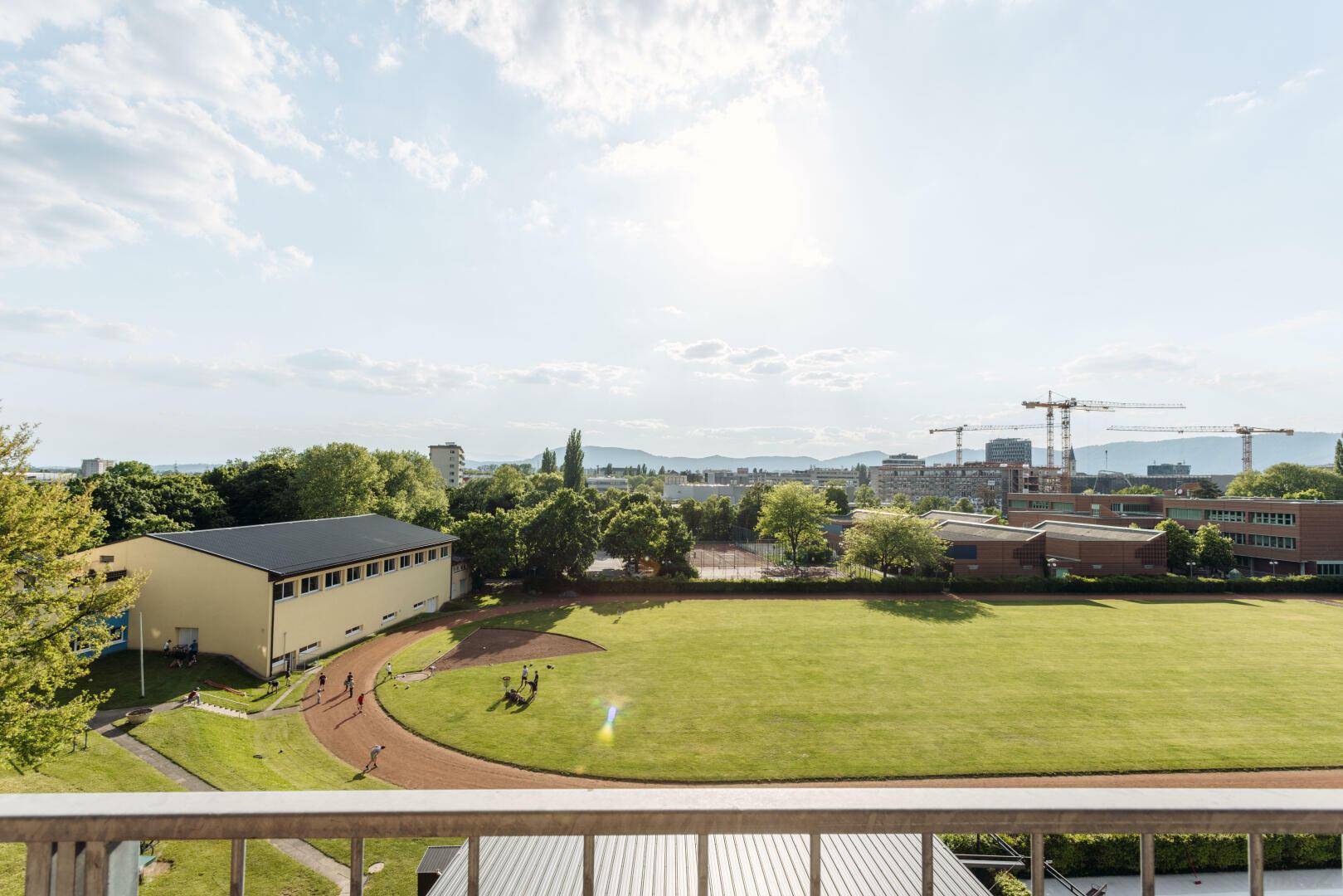 Weitblick von der Terrasse über eine grüne Sportanlage und die städtische Kulisse.