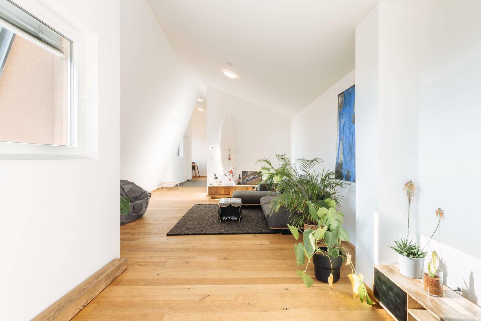 Geräumiges Wohnzimmer mit Holzboden, modernem Sofa und vielen grünen Pflanzen.