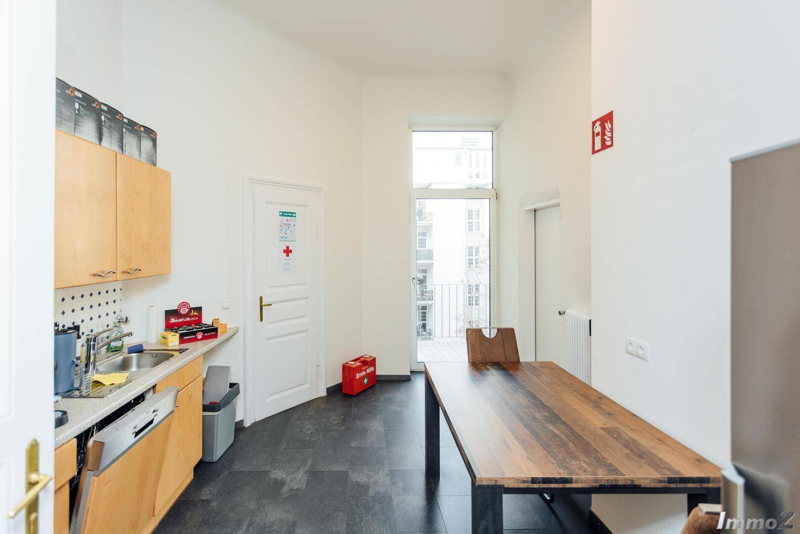 Funktionale Küche mit Holzschränken, Spüle und einem Esstisch mit Zugang zum Balkon, praktisch und hell.