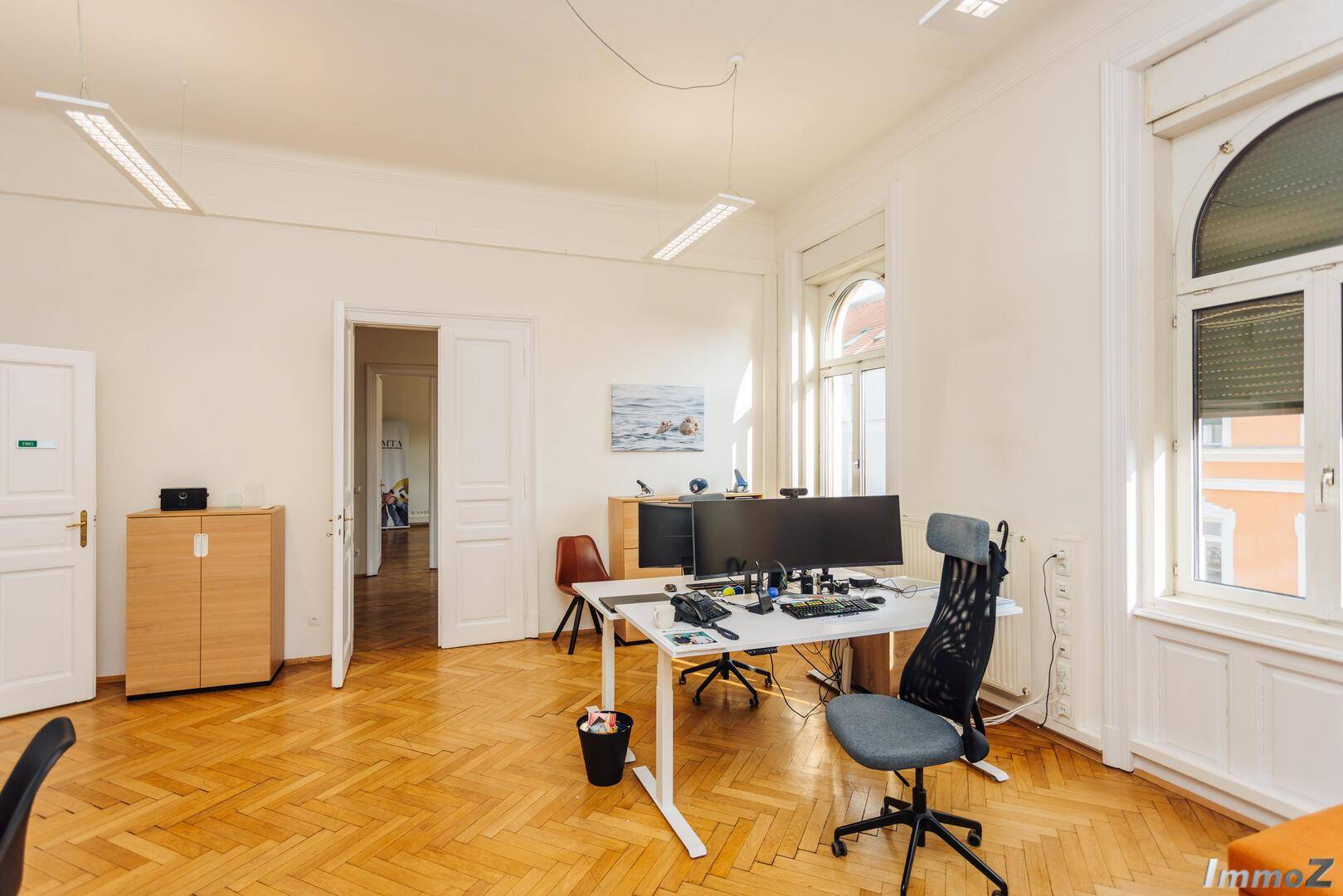 Helles Büro mit Fischgrätparkett, hohen Fenstern und modernen Arbeitsplätzen, ideal für konzentriertes Arbeiten.