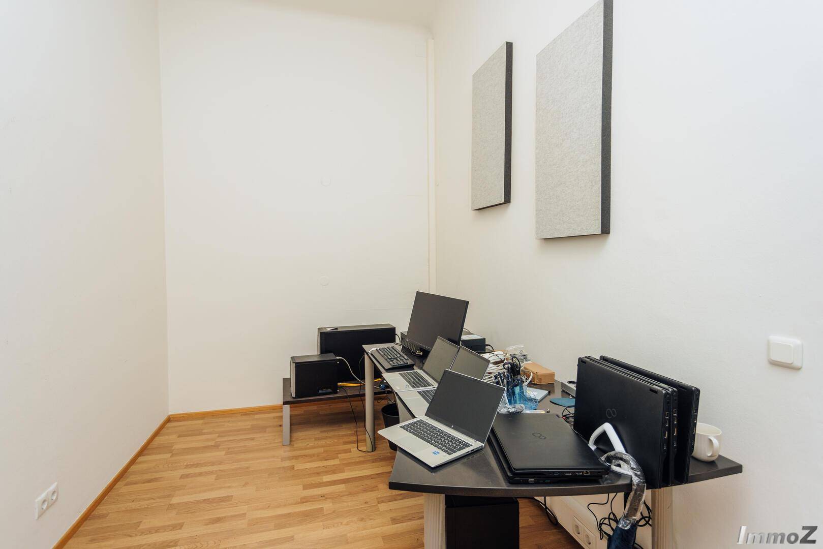 Kleiner Büroraum mit Laminatboden und mehreren Laptops auf einem Schreibtisch, funktional und kompakt.