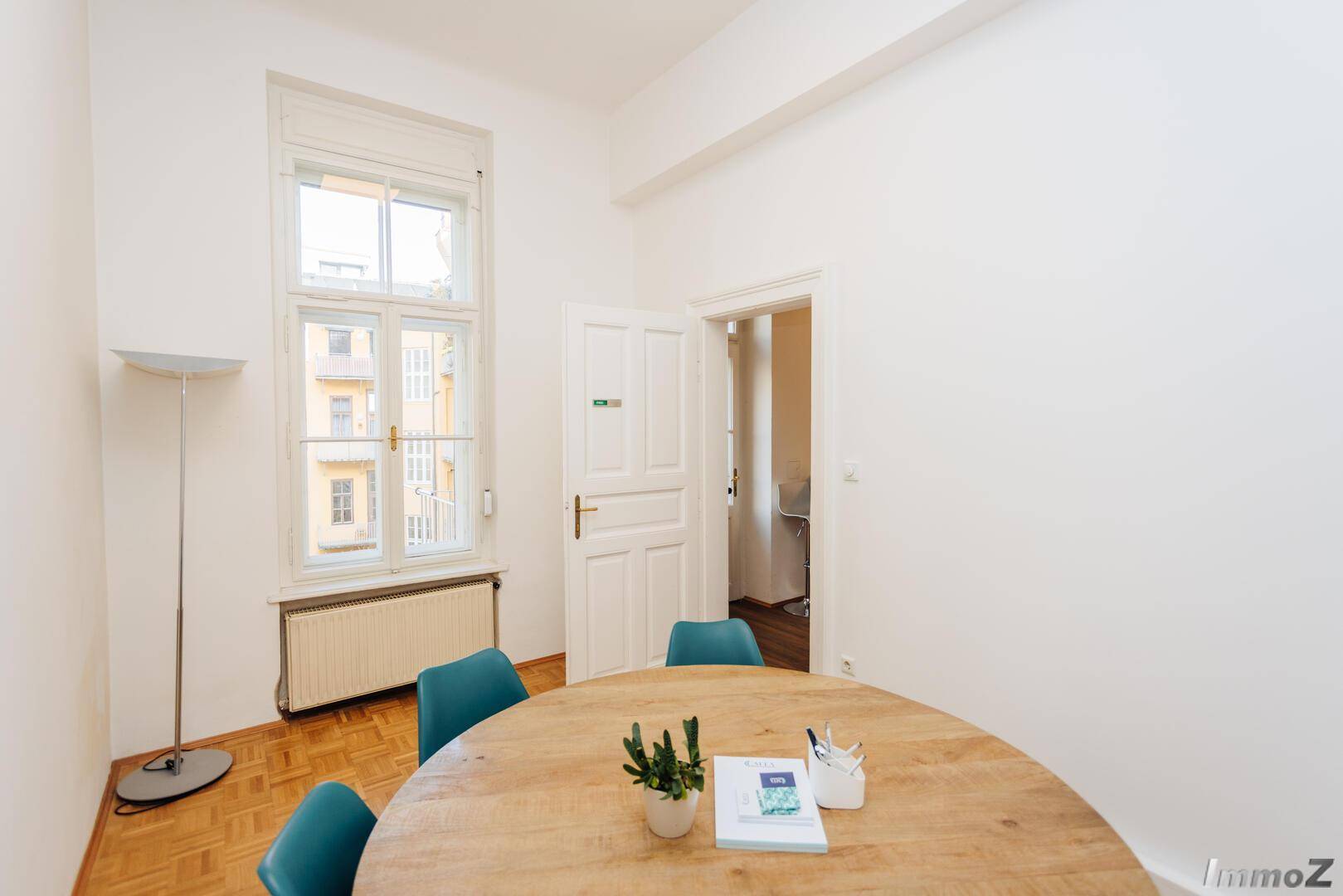 Kleiner Besprechungsraum mit Holztisch, blauen Stühlen und einem hohen Fenster mit Ausblick, ideal für kleine Teams.