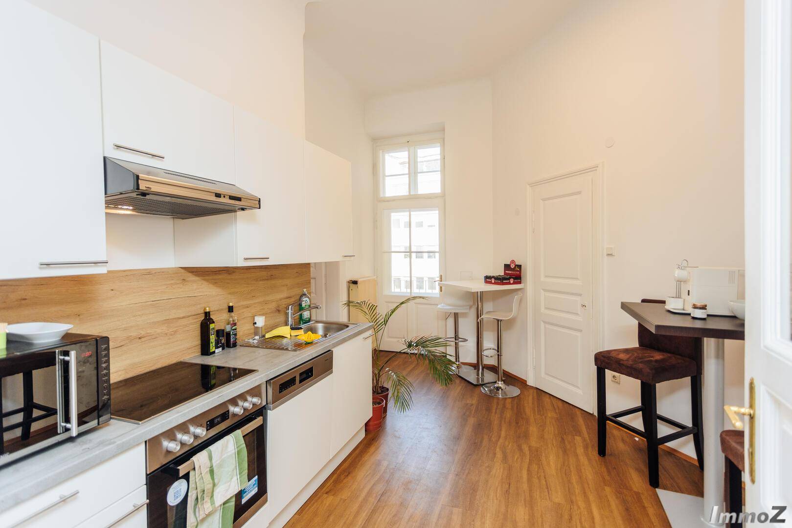 Moderne weiße Küche mit Holzakzenten, Induktionskochfeld und einem kleinen Essbereich, funktional und hell gestaltet.