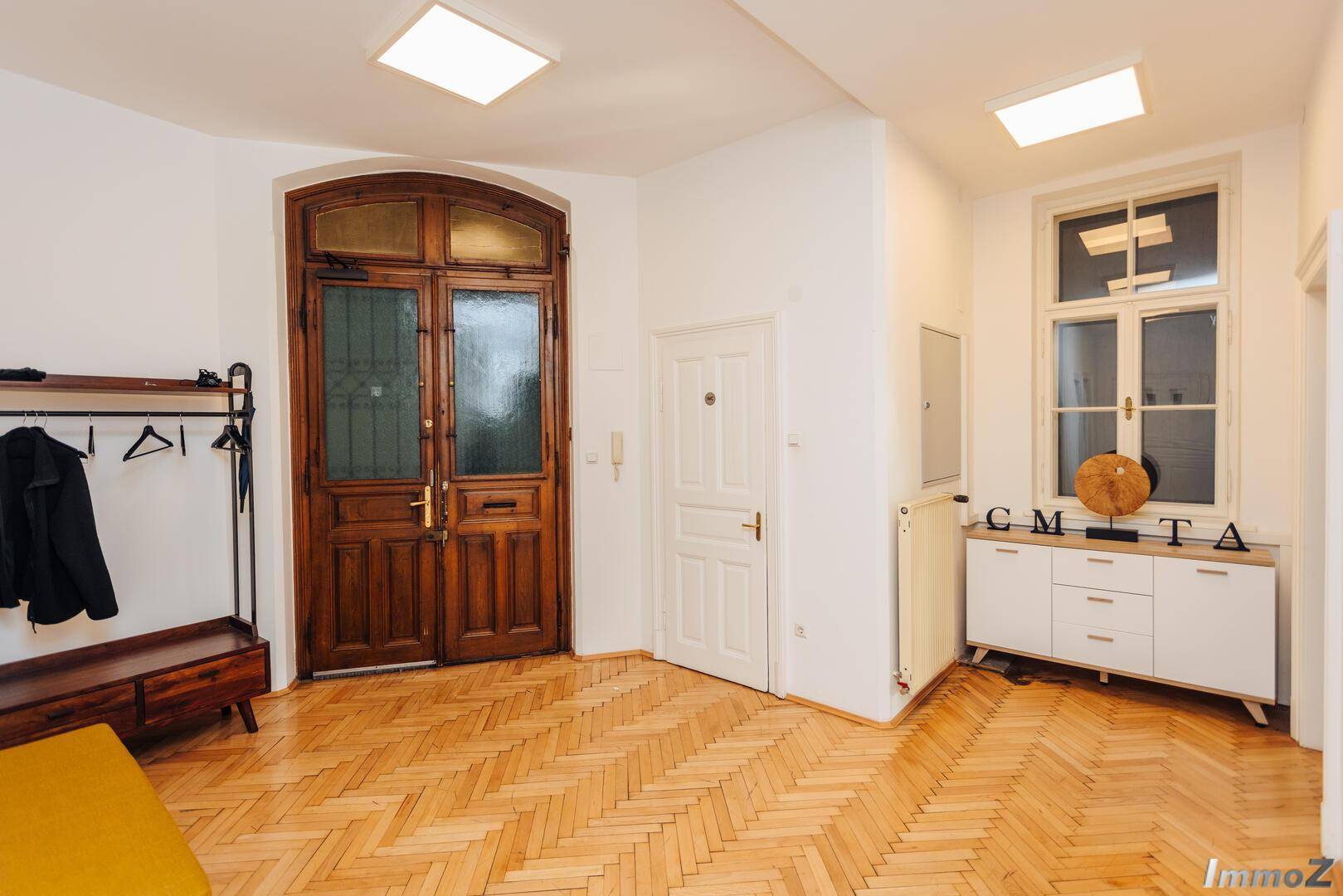 Geräumiger Eingangsbereich mit Fischgrätparkett, einer großen Holztür und einem modernen Sideboard, das zum Verweilen einlädt.
