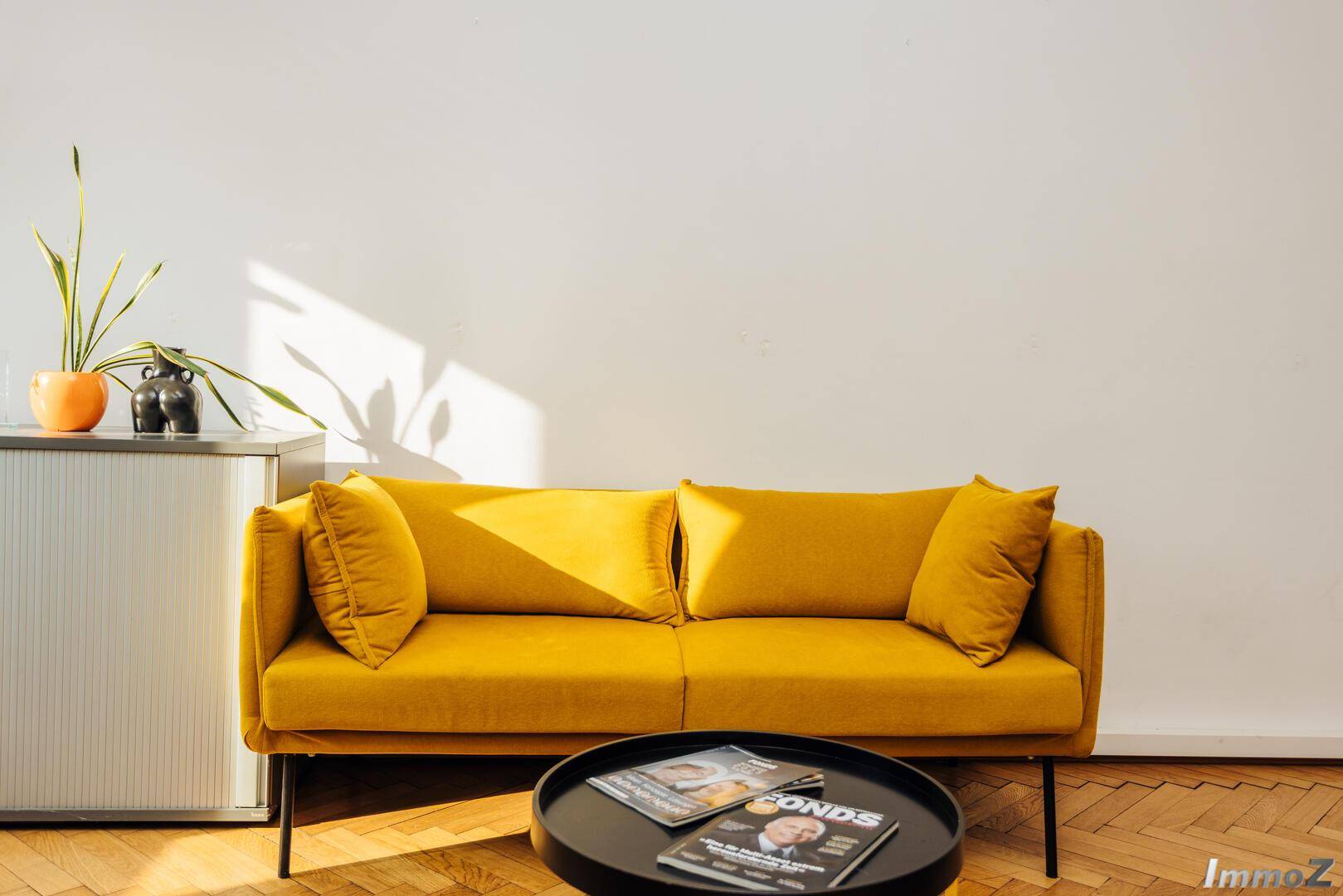 Gemütliches gelbes Sofa mit Beistelltisch und Magazinen in einem hellen Bürobereich, perfekt für eine kurze Pause.