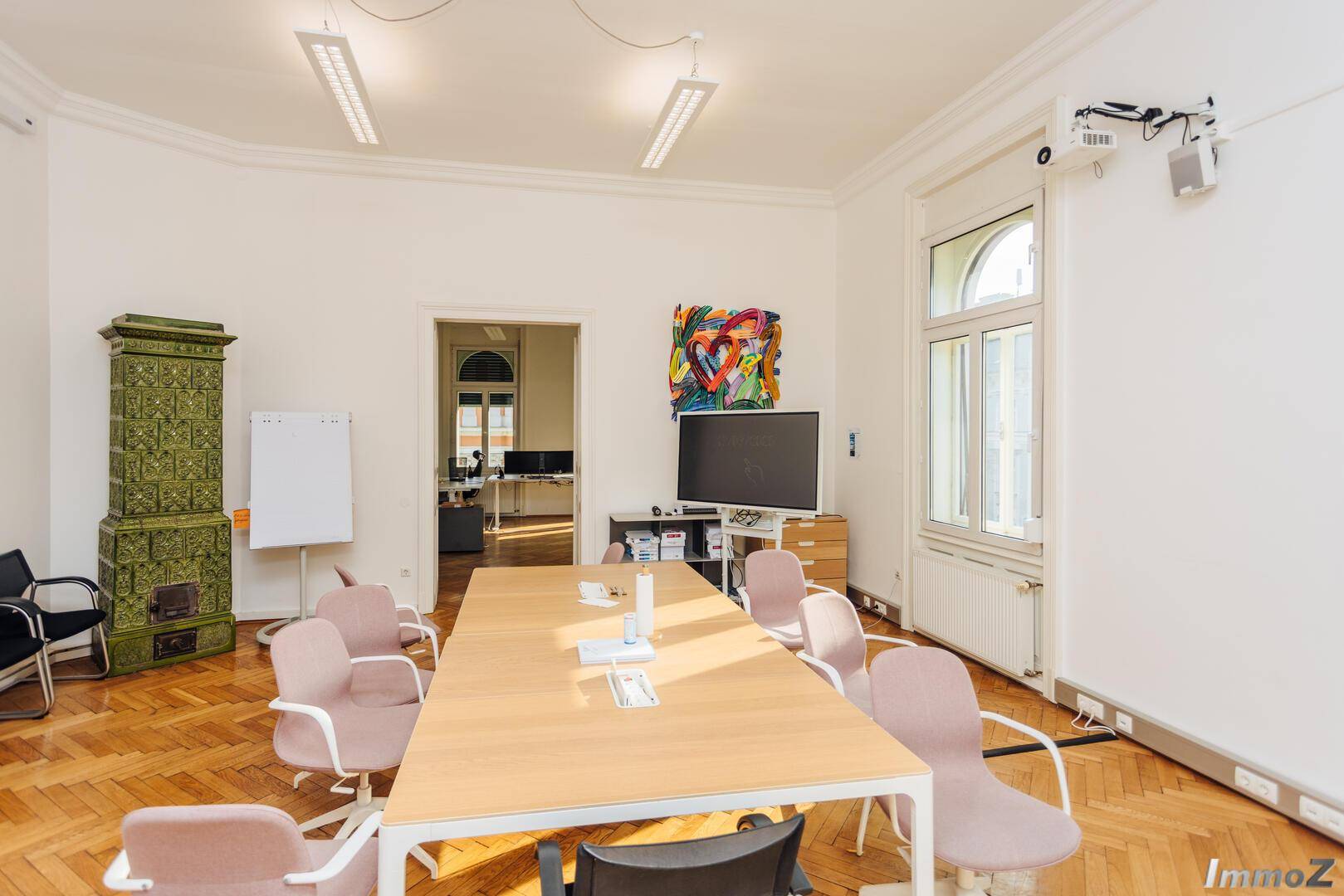 Großer Konferenzraum mit Holzboden, hohen Fenstern und einem traditionellen Kachelofen, ideal für produktive Meetings.