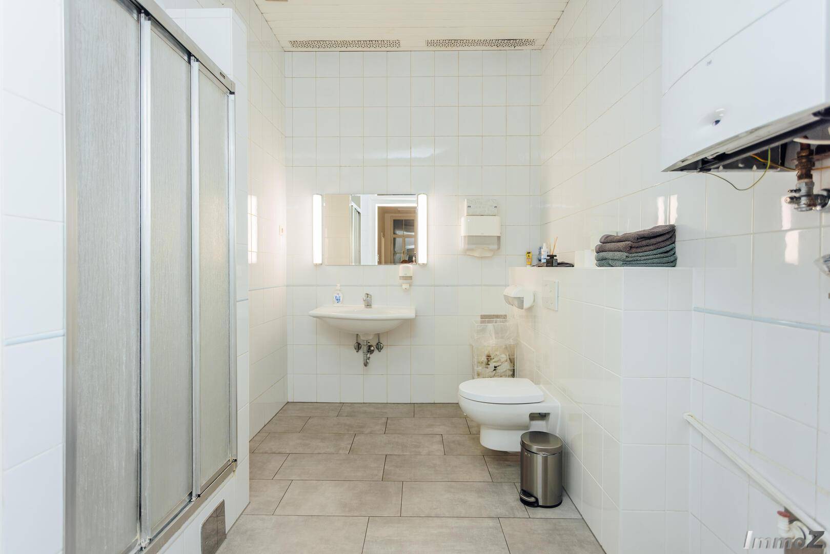 Helles Badezimmer mit weißen Fliesen, Duschkabine und einem wandhängenden WC, modern und funktional ausgestattet.