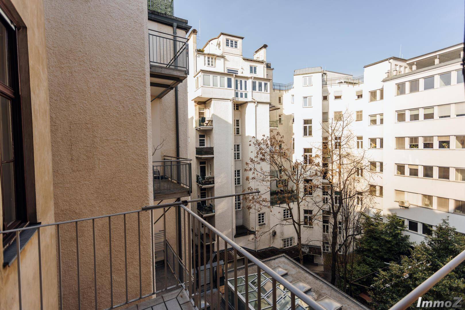 Blick vom Balkon auf einen ruhigen Innenhof mit mehreren Gebäuden und Bäumen, bietet eine grüne Oase.