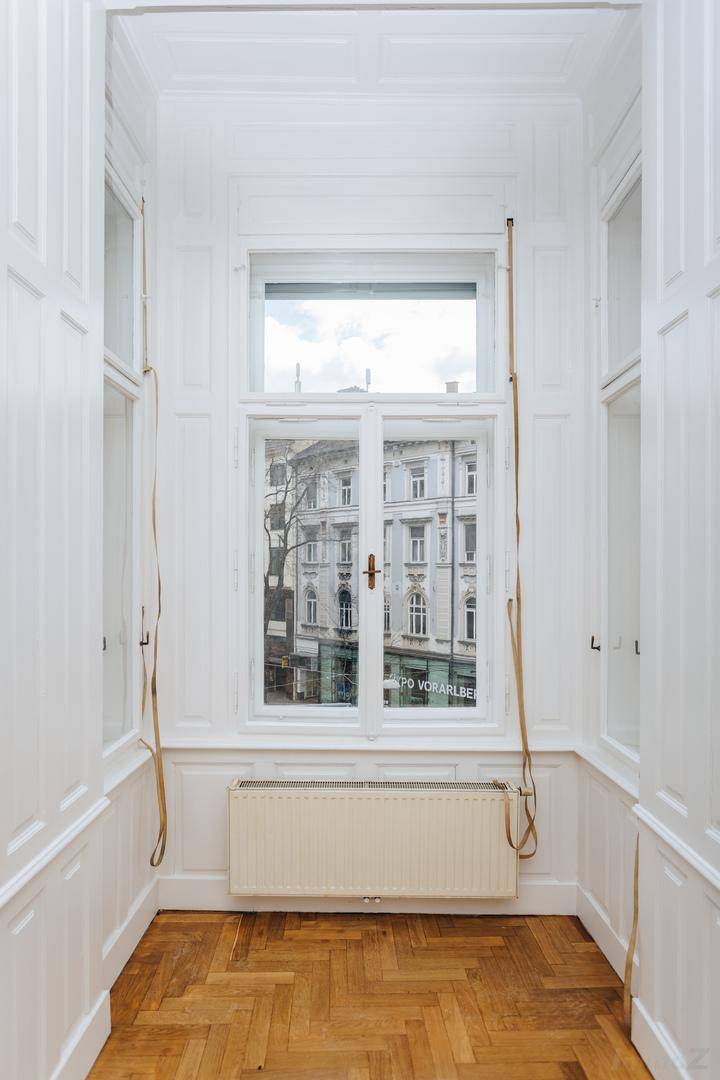 Heller Erkerbereich mit Fischgrätparkett und einem hohen Fenster, das den Blick auf die Stadt freigibt.