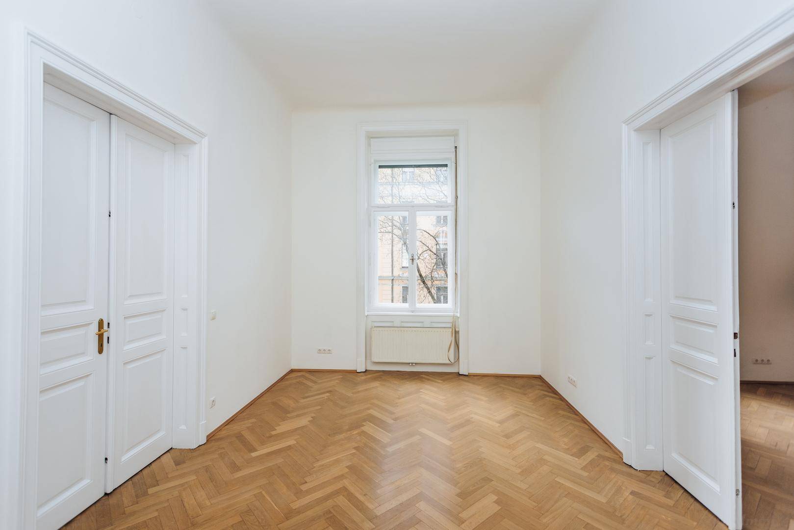 Geräumiger Raum mit Fischgrätparkett und einem hohen Fenster, das viel natürliches Licht spendet.