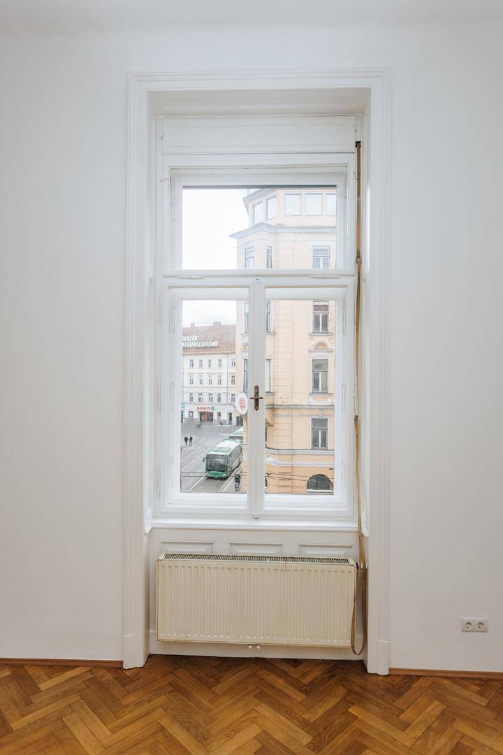 Hohes Fenster mit Blick auf die Stadtstraße und ein vorbeifahrendes Fahrzeug, mit Heizkörper darunter.