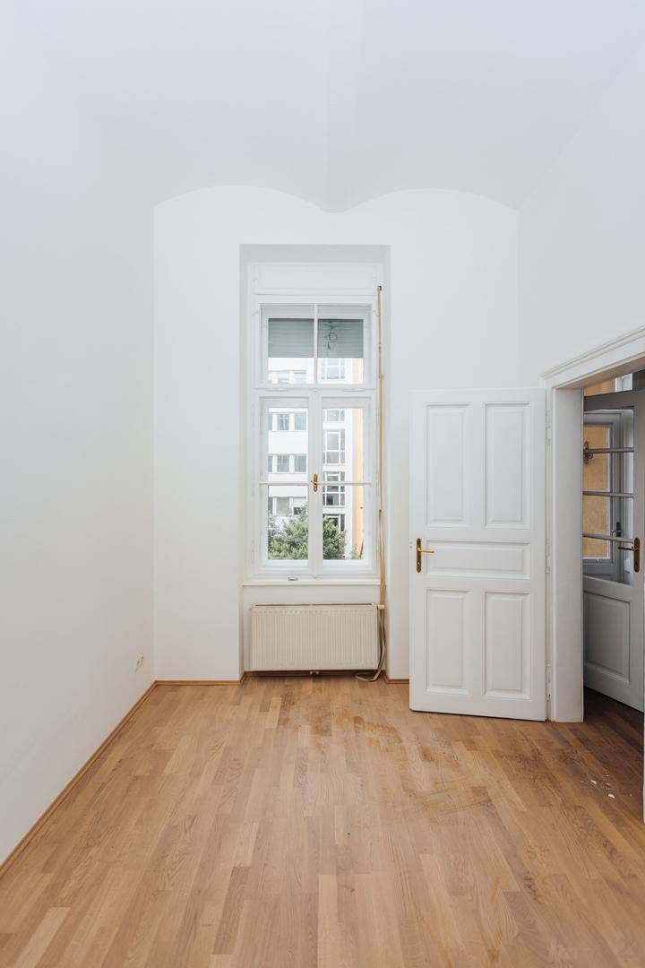 Heller Raum mit Fischgrätparkett und einem hohen Fenster, das den Blick nach draußen freigibt.