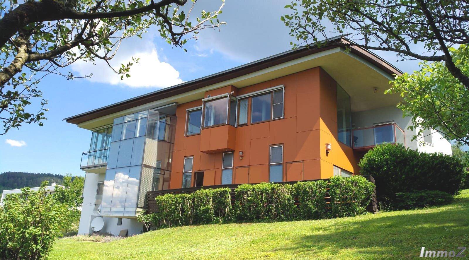 Moderne Architektur des Hauses mit orangefarbener Fassade und großen Fenstern.