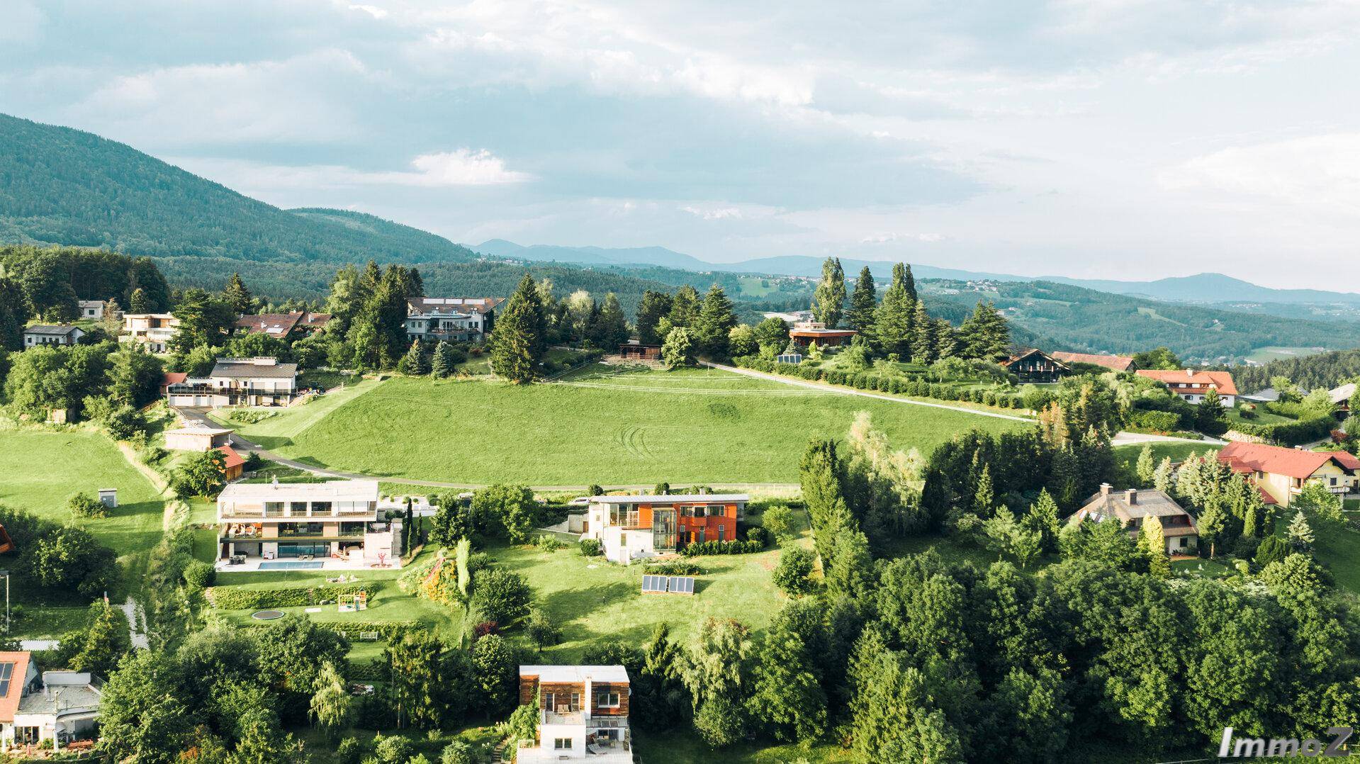 Luftaufnahme einer Wohnsiedlung in grüner Hügellandschaft mit modernen Häusern.