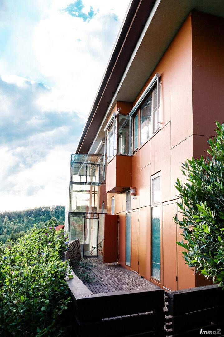 Holzterrasse mit Blick ins Grüne, umgeben von Hecken und moderner Architektur.