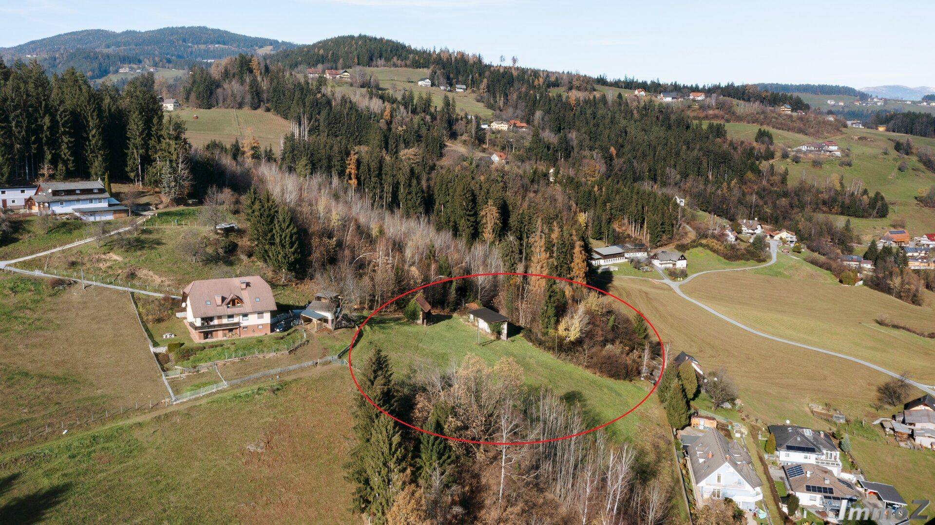 Luftaufnahme eines Grundstücks in hügeliger Landschaft, umgeben von Wald und weiteren Wohnhäusern, mit weitem Blick.