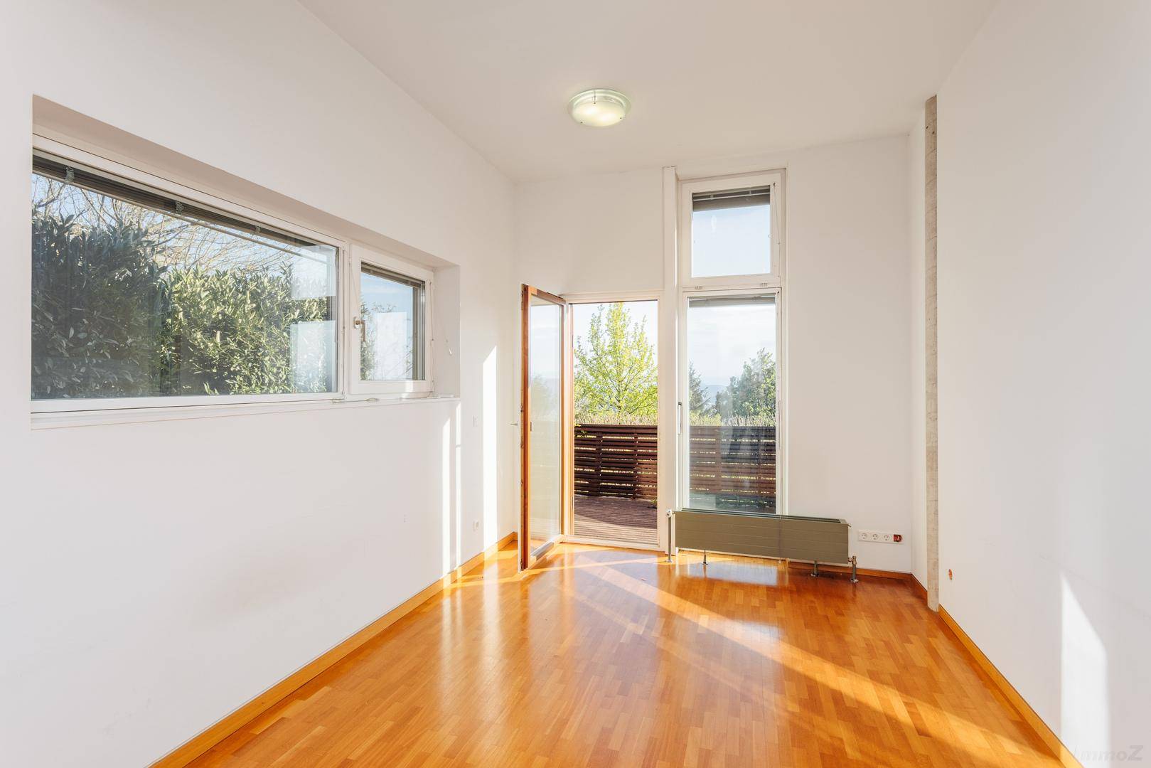 Helles Zimmer mit Holzboden und Zugang zu einem Balkon, ideal als Schlaf- oder Arbeitszimmer.
