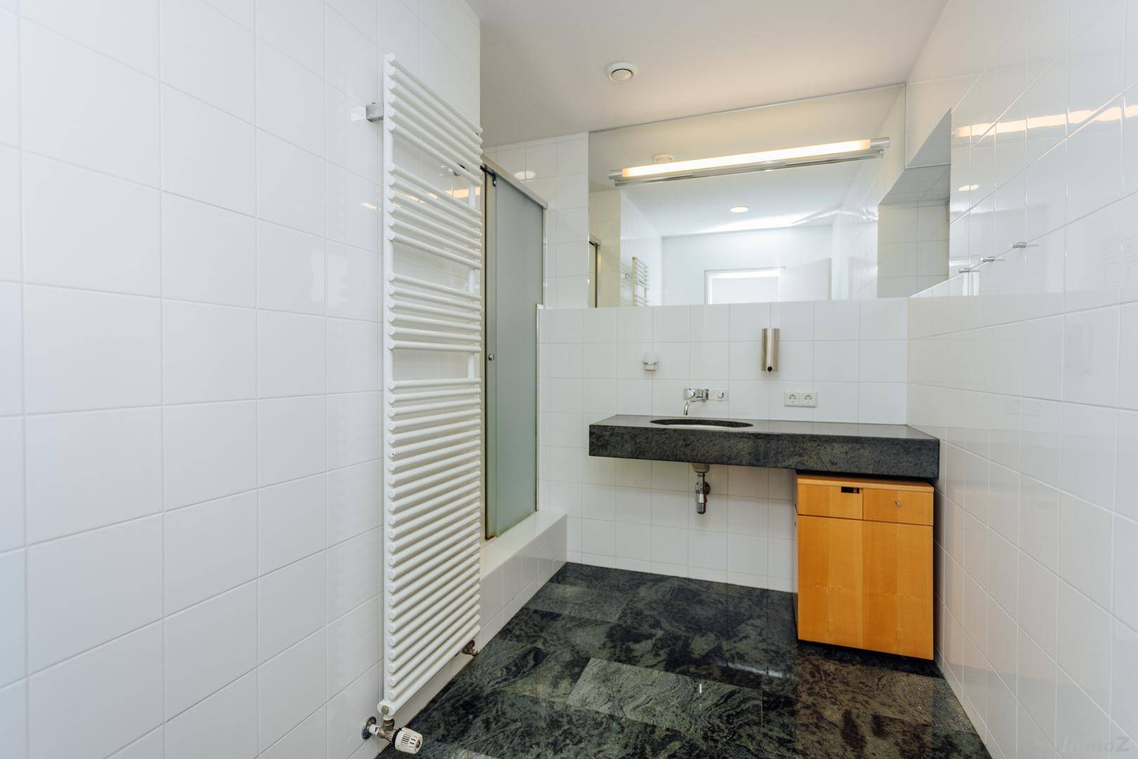 Modernes Badezimmer mit weißen Fliesen, dunklem Steinboden und beheiztem Handtuchhalter.