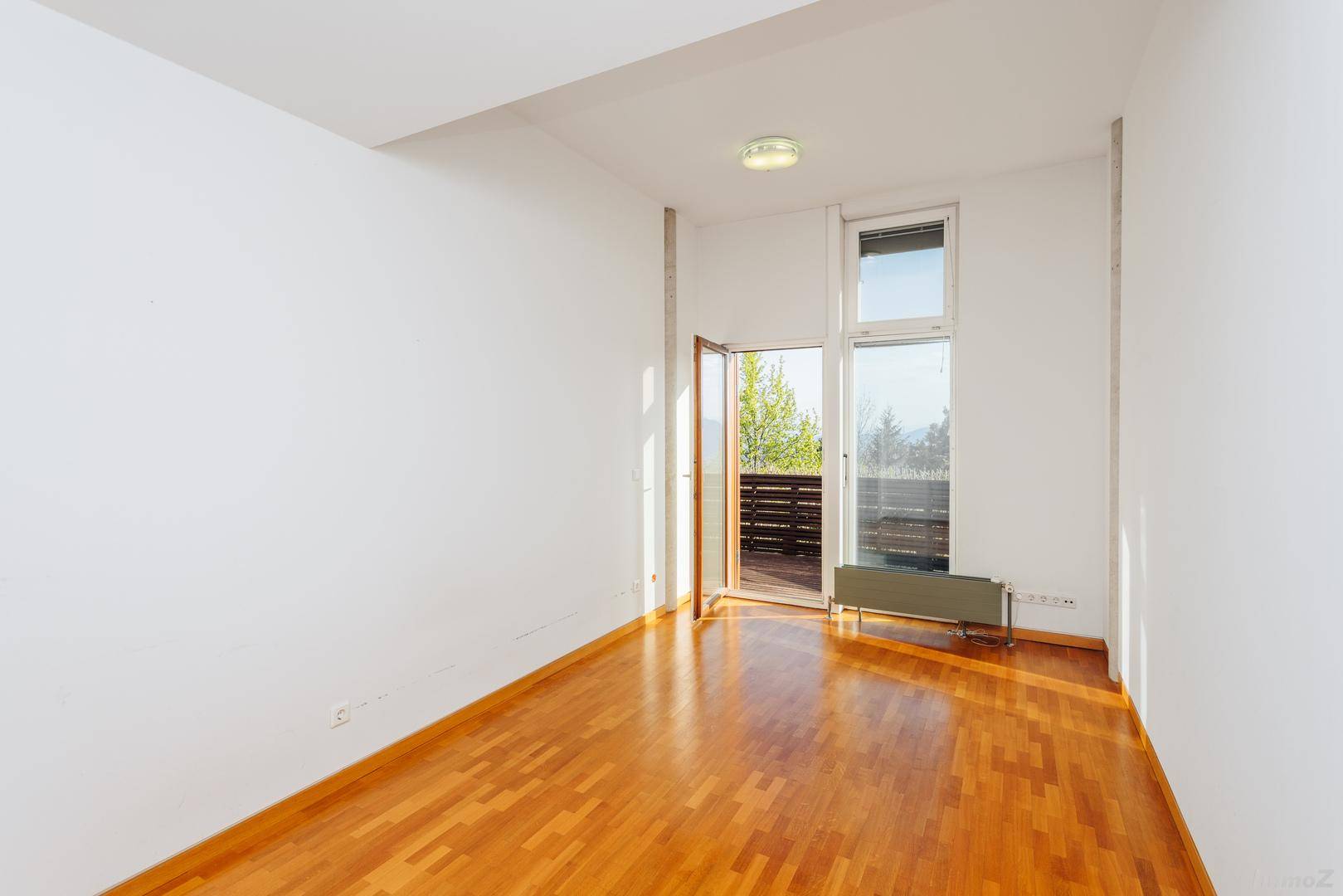 Helles Zimmer mit Holzboden und Balkonzugang, vielseitig nutzbar als Schlaf- oder Gästezimmer.