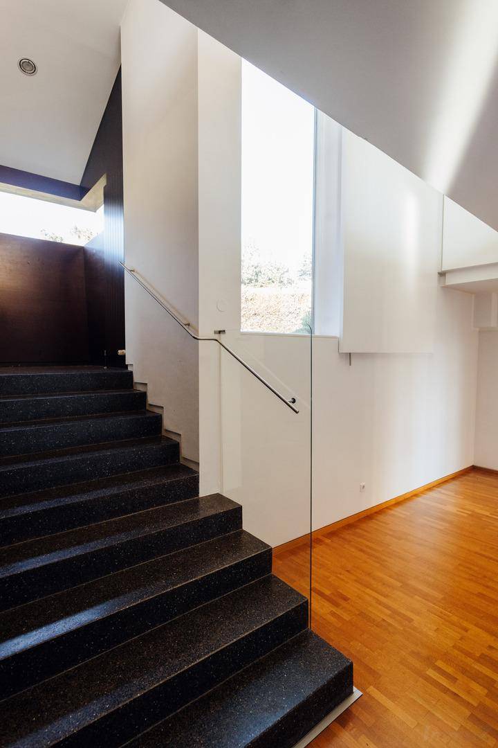 Moderner Treppenaufgang mit dunklen Stufen, Glasgeländer und heller Wandgestaltung.