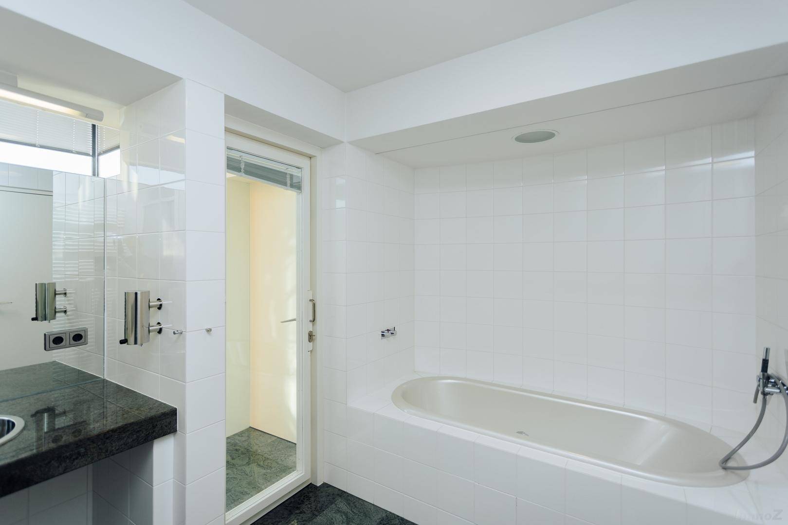 Modernes Badezimmer mit Badewanne, weißen Fliesen und dunklem Steinboden.