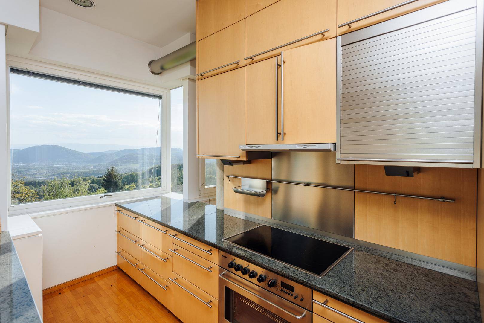 Moderne Küche mit Holzschränken, Granitarbeitsplatte und Fenster mit weitem Landschaftsblick.