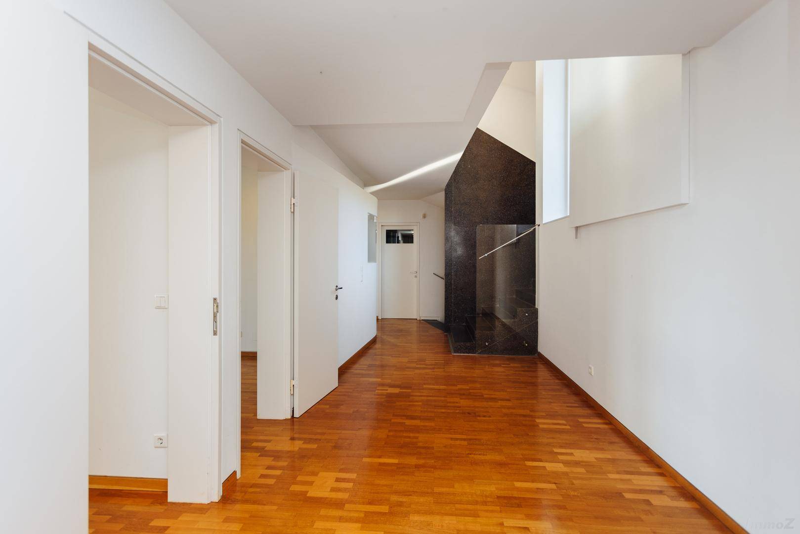 Geräumiger Flur mit Holzboden und weiß gestrichenen Wänden, der zu weiteren Räumen führt.