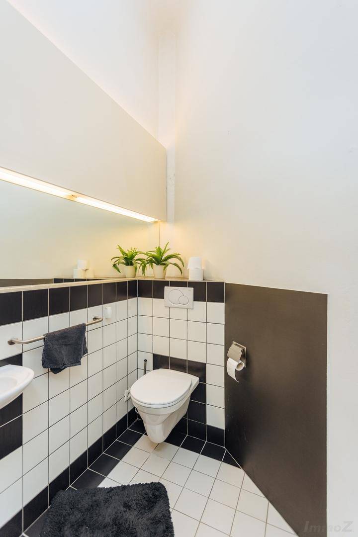 Gästetoilette mit schwarz-weißen Fliesen, wandhängendem WC und kleinem Waschbecken.