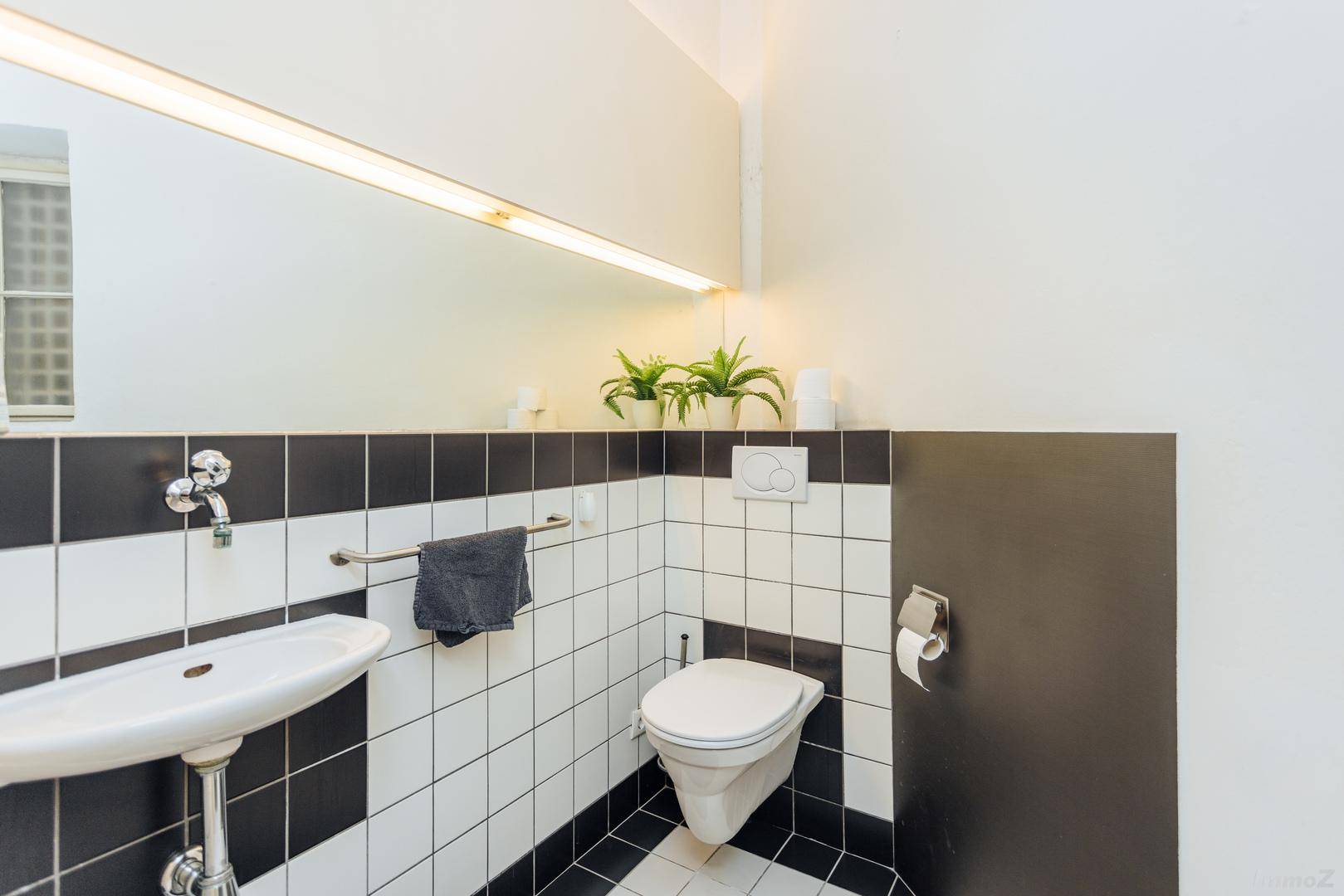 Modern geflieste Gästetoilette in Schwarz-Weiß mit Waschbecken und Spiegel, gut beleuchtet.