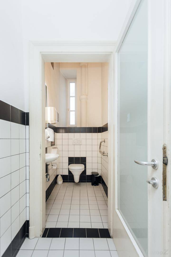 Schmale Gästetoilette mit schwarz-weißen Fliesen, kleinem Waschbecken und Fenster.