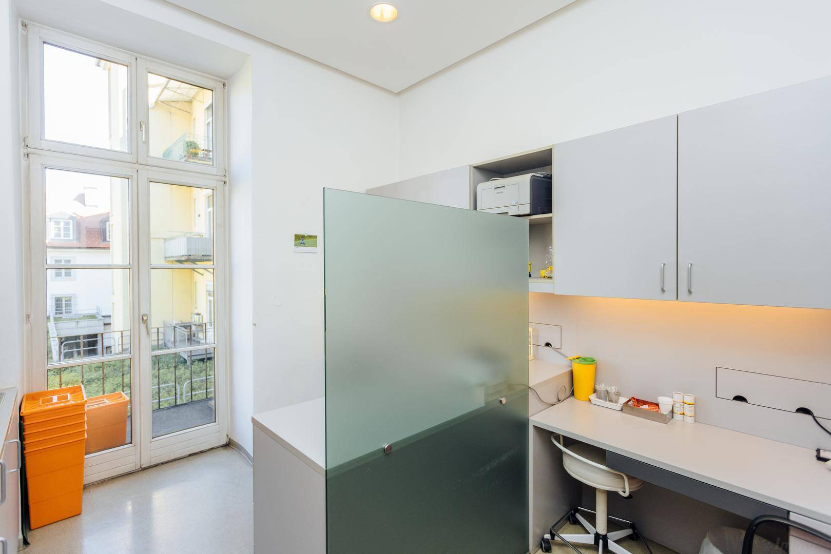 Laborbereich mit grauen Schränken, Arbeitsfläche und Zugang zu einem Balkon oder einer Terrasse.