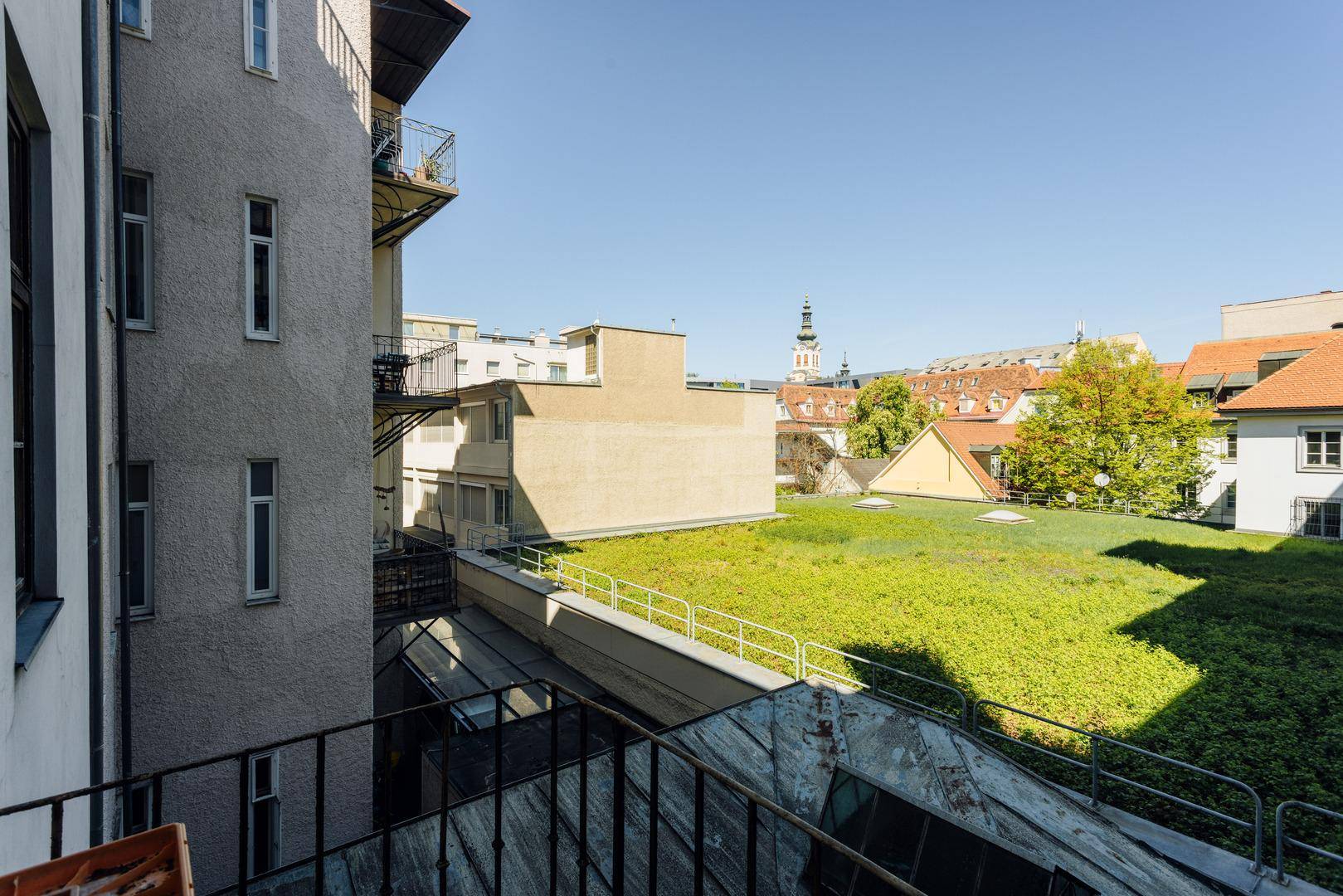 Blick von einem Balkon auf begrünte Dächer und die umliegende Stadtlandschaft.