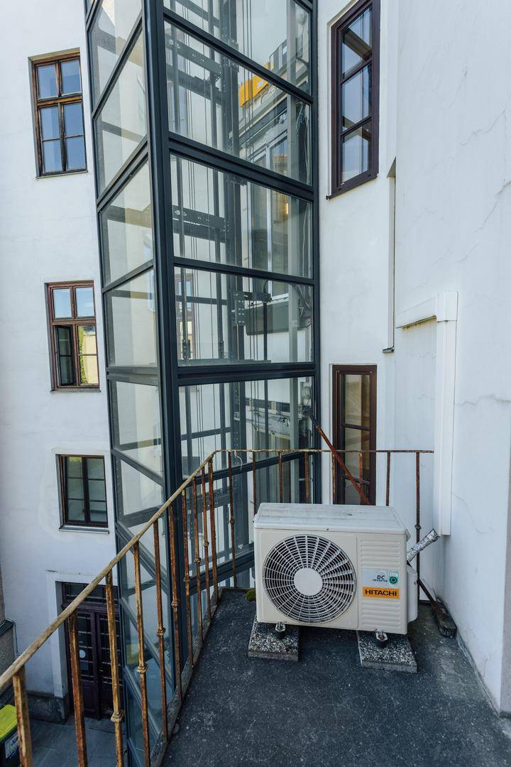 Außenansicht eines Gebäudes mit einem modernen Glasaufzug und einer Klimaanlage.