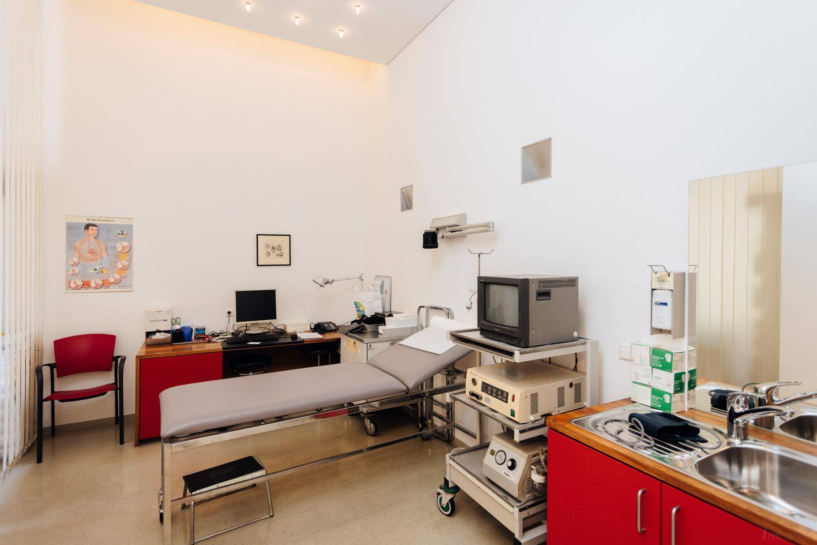 Untersuchungszimmer mit medizinischer Ausstattung, Waschbecken und vielen Deckenleuchten.