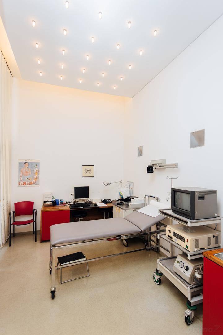 Helles Untersuchungszimmer mit medizinischer Liege, Waschbecken und zahlreichen Deckenstrahlern.