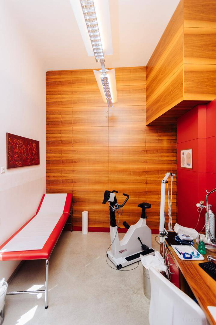 Modernes Untersuchungszimmer mit Holzverkleidung, medizinischer Liege und Trainingsgerät.