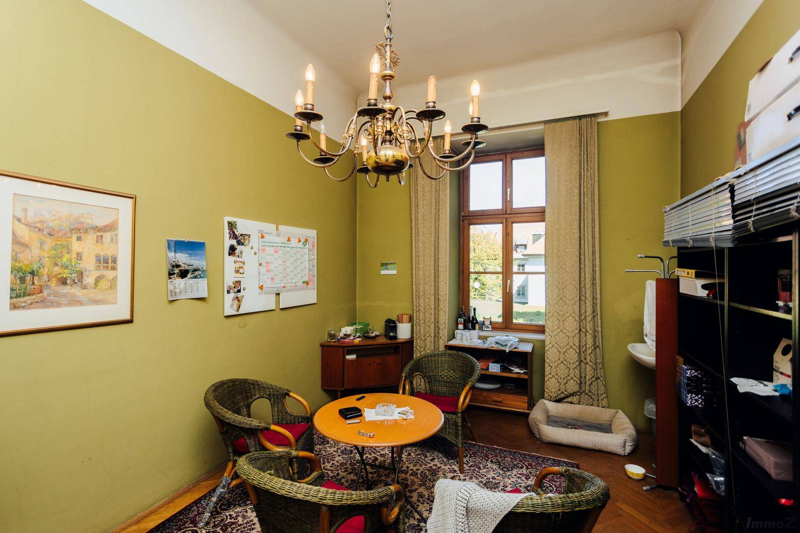 Büro mit olivgrünen Wänden, Korbmöbeln und einem Kronleuchter, gemütlich eingerichtet.