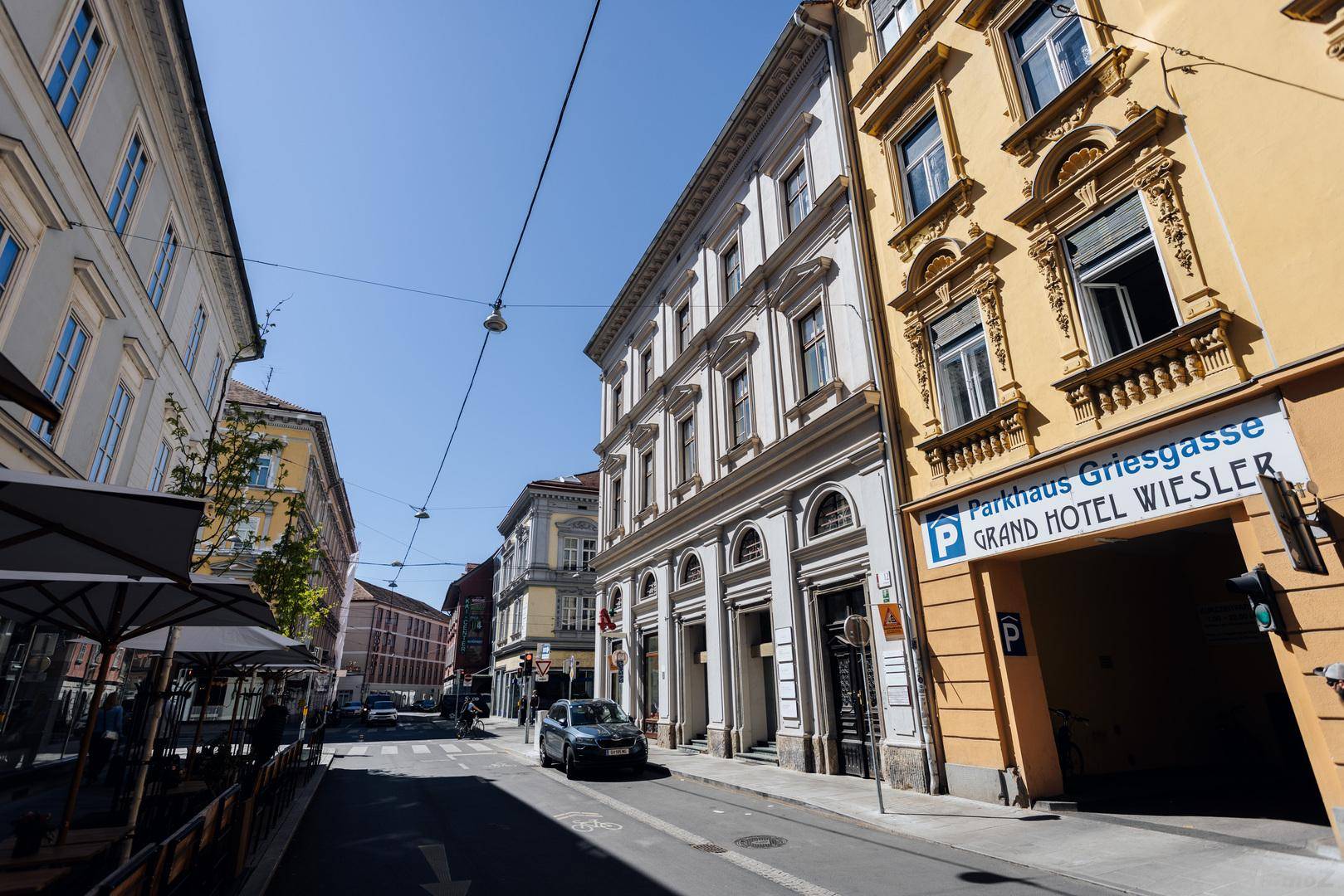 Belebtes Stadtbild mit historischen Gebäuden, Geschäften und einem Parkhaus unter blauem Himmel.