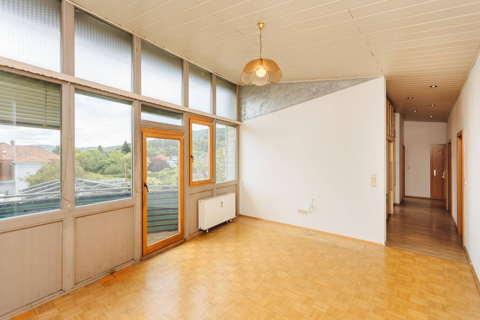 Heller, leerer Raum mit vielen Fenstern und Holzboden, ideal als Wintergarten oder Wohnbereich.