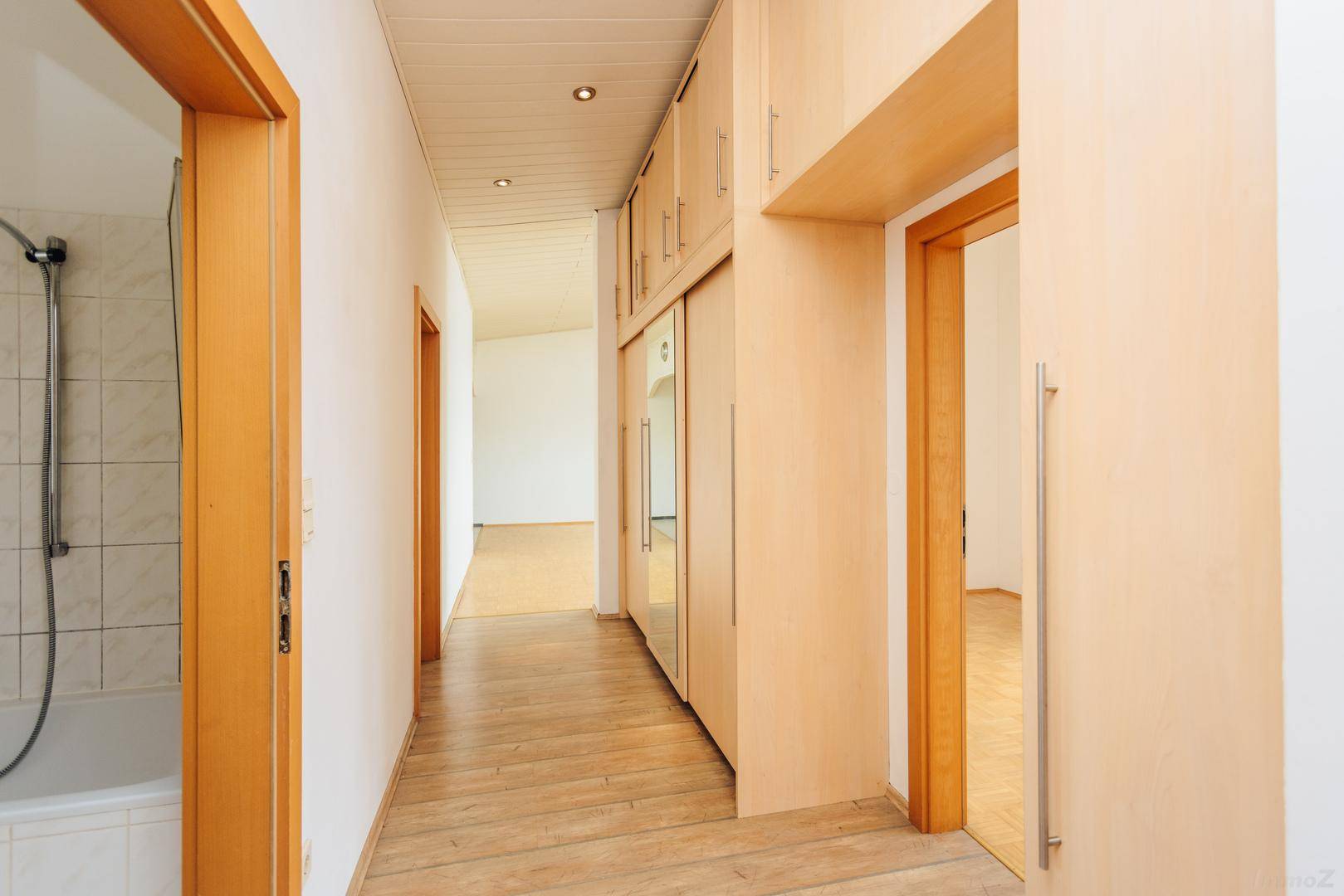 Langer Flur mit Holzboden, Einbauschränken und Zugang zu verschiedenen Zimmern der Wohnung.
