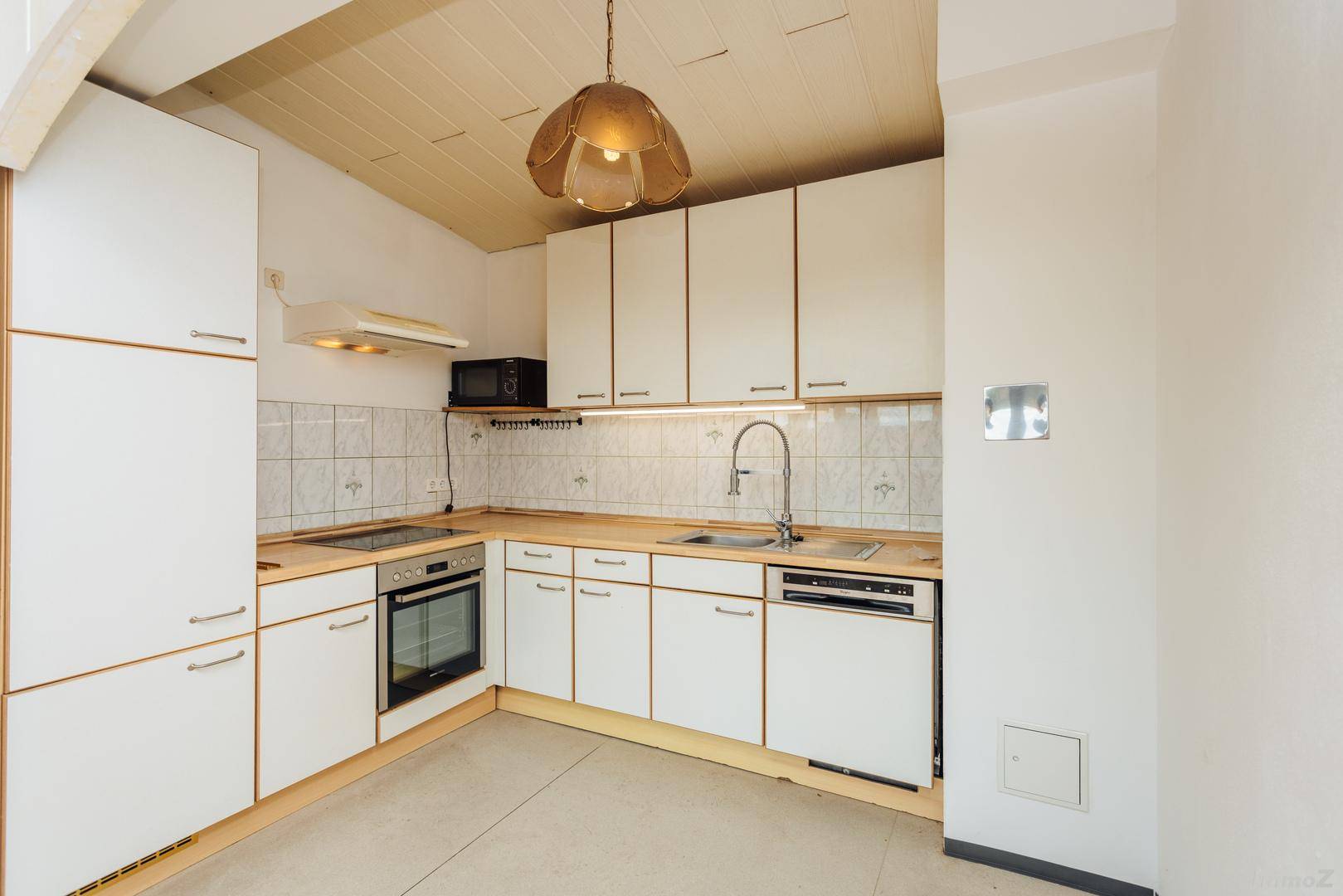 Helle Einbauküche mit weißen Schränken, Holztheke und integrierten Geräten unter Dachschräge.