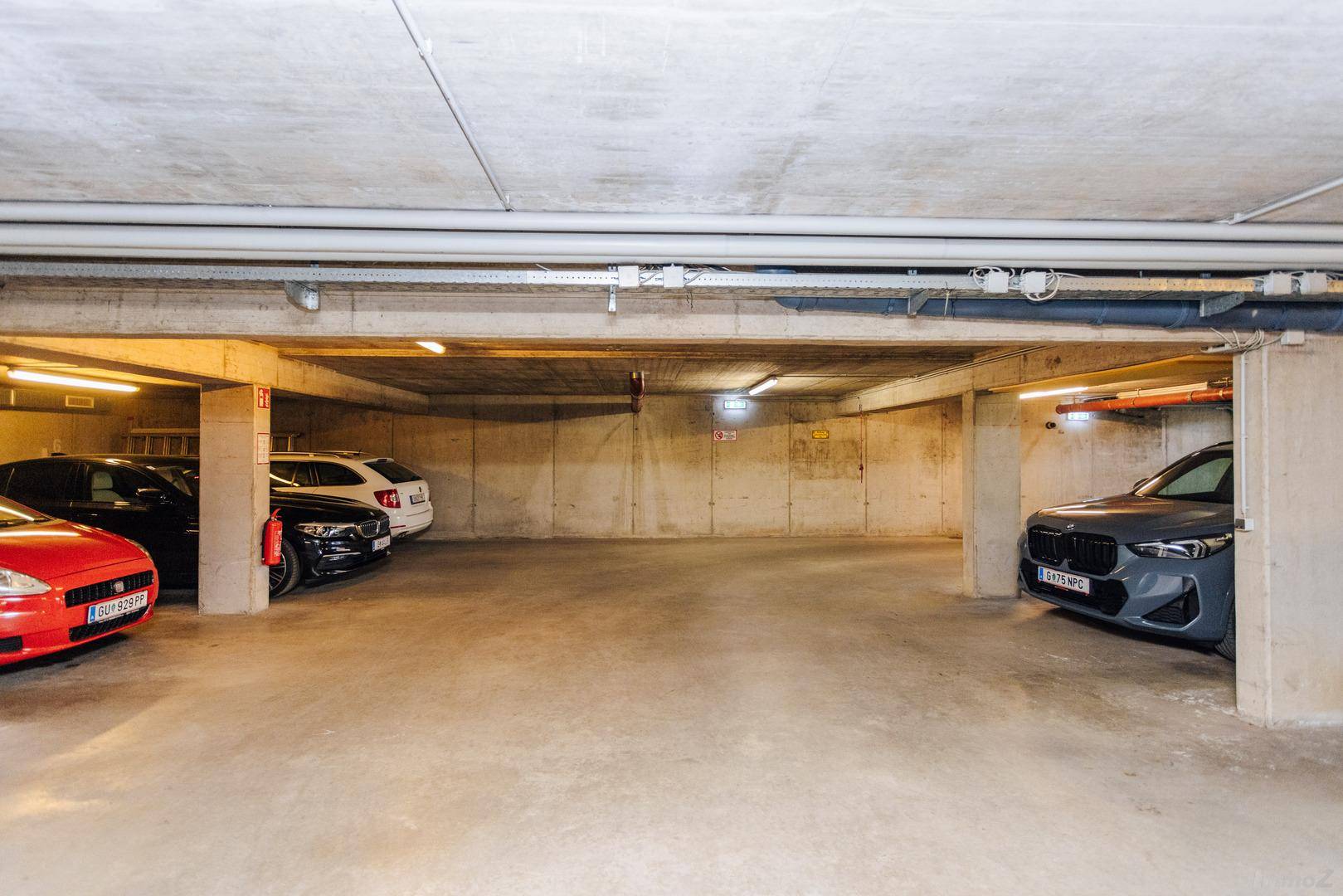 Geräumige Tiefgarage mit mehreren Stellplätzen und Betonwänden, gut beleuchtet.