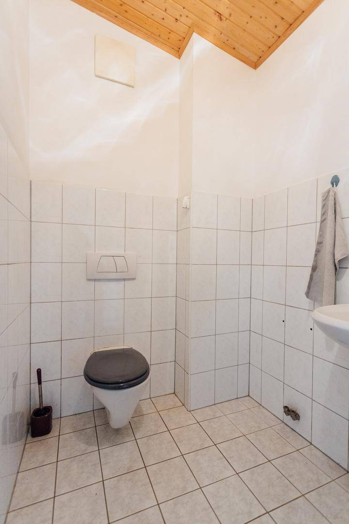 Kleines Gäste-WC mit Wand-WC, Waschbecken und weißen Fliesen, mit Holzdecke.