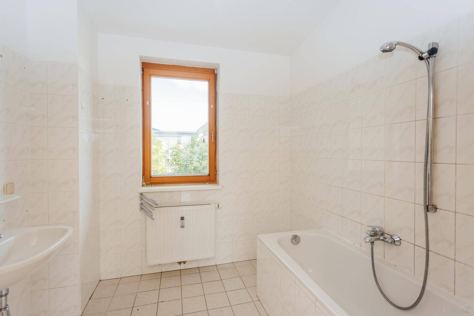 Helles Badezimmer mit Badewanne, Waschbecken und Fenster, gefliest in neutralen Farben.